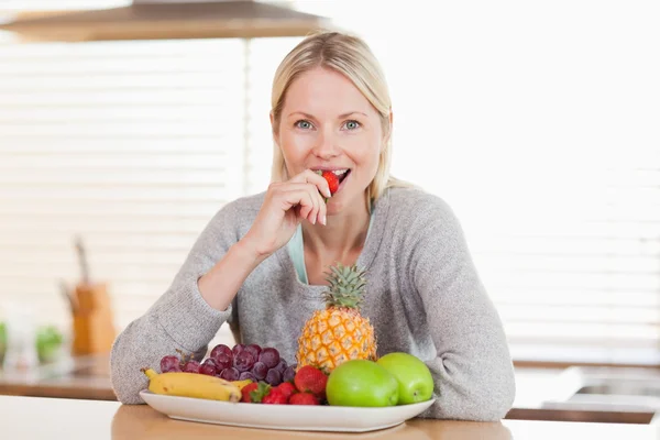 Mujer en la cocina comiendo una fresa — Foto de Stock