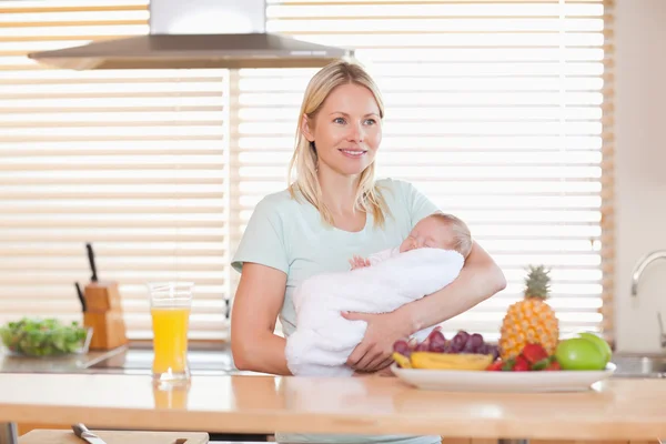 Woman standing in the kitchen holding her baby — Stock Photo, Image