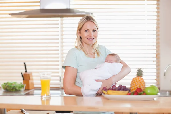 Woman standing in the kitchen while holding her baby — Stock Photo, Image
