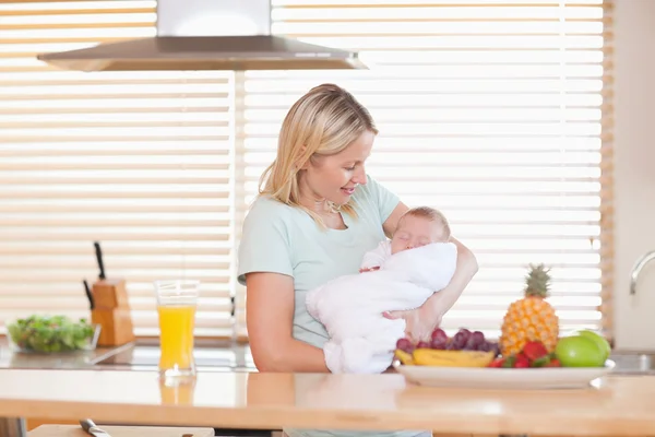 Женщина держит спящего ребенка на кухне — стоковое фото