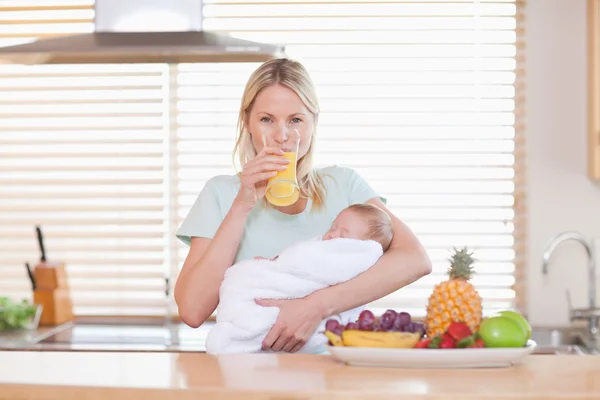 Woman drinking juice while holding her baby — Stock Photo, Image