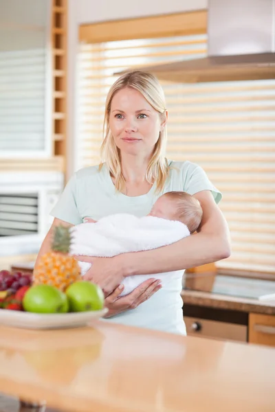 Mujer de pie en la cocina con su bebé en sus brazos — Foto de Stock