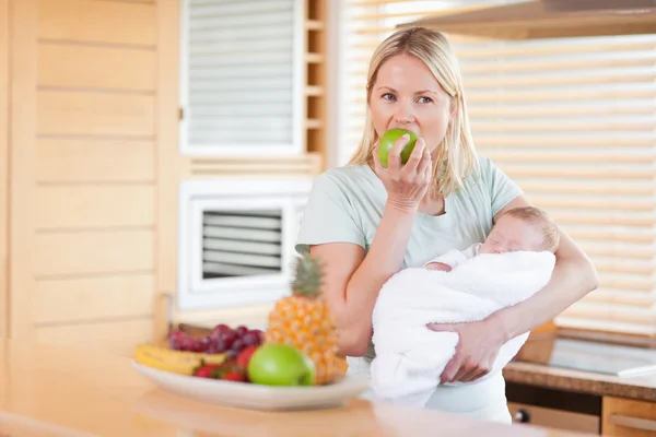 Kvinna med baby på hennes armar äta ett äpple — Stockfoto