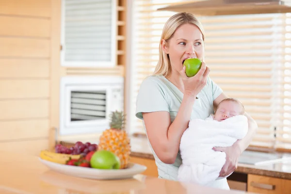 Frau beißt mit Baby auf dem Arm in Apfel — Stockfoto