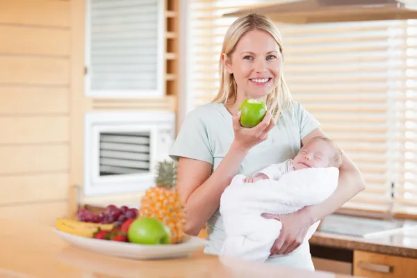 Mulher sorridente com uma maçã e seu bebê em seus braços — Fotografia de Stock