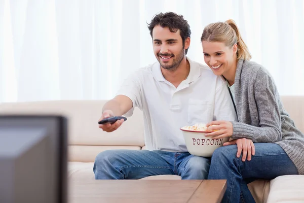 Улыбающаяся пара смотрит телевизор, когда ест попкорн — стоковое фото