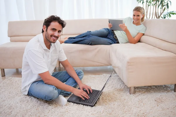 Mulher usando um computador tablet enquanto seu namorado está usando um não — Fotografia de Stock