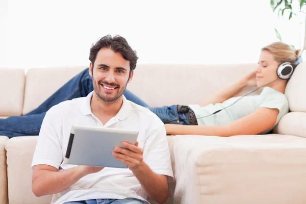 Człowiek za pomocą komputera typu tablet, a jego żona jest słuchanie muzyki — Zdjęcie stockowe