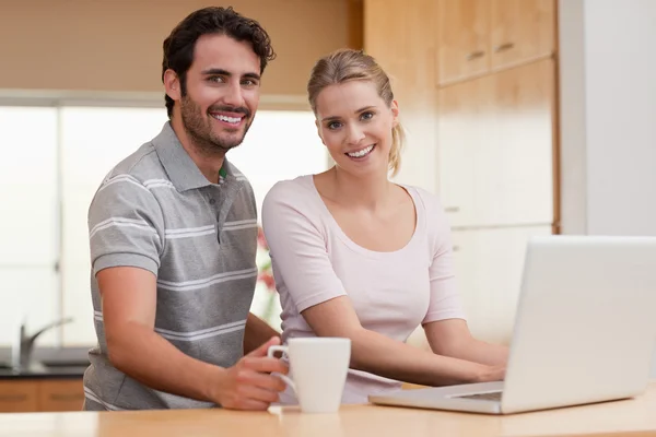 Smiling couple using a notebook while having coffee — Stock Photo, Image