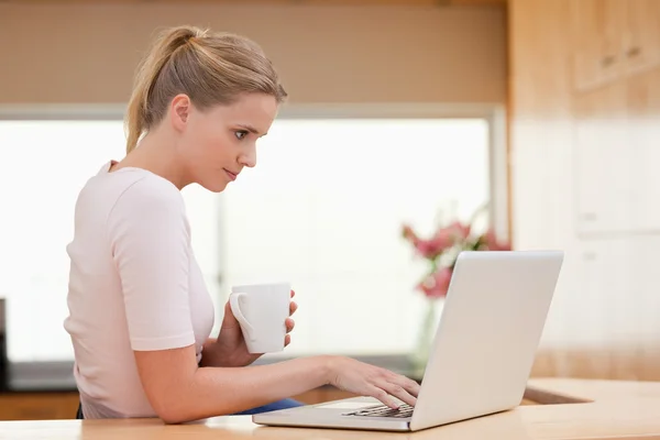 女人喝一杯茶的同时使用一台笔记本电脑 — 图库照片