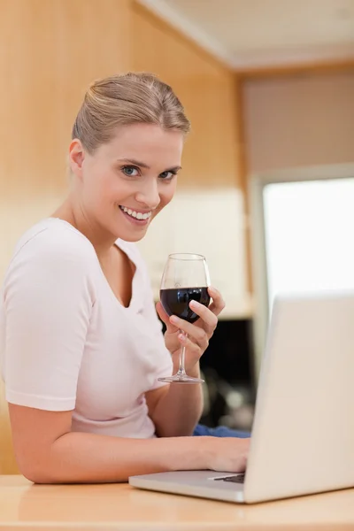 Retrato de uma mulher usando um laptop enquanto bebe vinho tinto — Fotografia de Stock