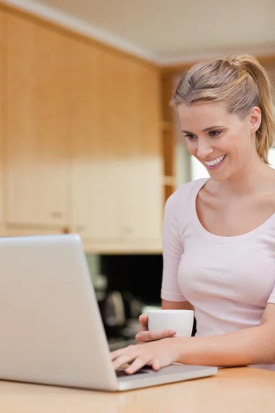 Portrait of a woman using a laptop while drinking tea — Stock Photo, Image