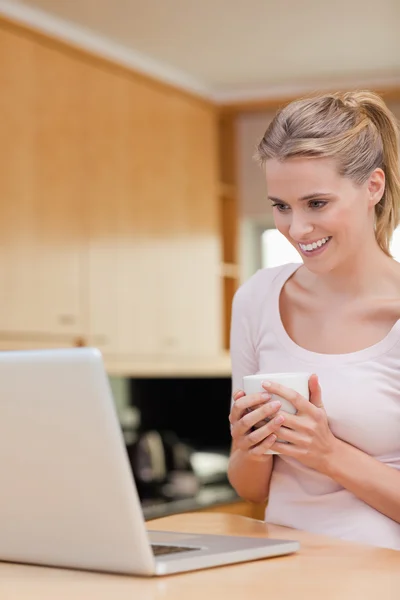 Retrato de una mujer joven usando un ordenador portátil mientras bebe café —  Fotos de Stock
