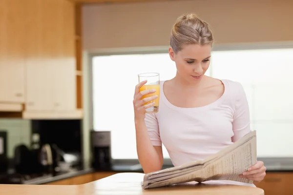 Женщина читает новости, когда пьет апельсиновый сок — стоковое фото