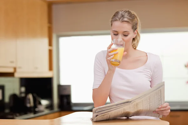 Jonge vrouw lezen van het nieuws terwijl het drinken sinaasappelsap — Stockfoto