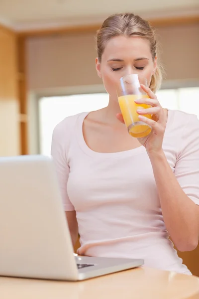 Retrato de uma jovem mulher usando um laptop enquanto bebe suco — Fotografia de Stock