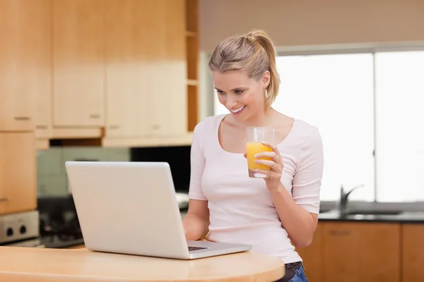 Woman using a laptop while drinking juice — Stock Photo, Image