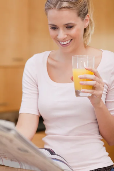 Porträtt av en ung kvinna läsa nyheter och dricka juice — Stockfoto