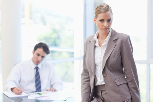 Geschäftsfrau posiert, während ihr Kollege arbeitet — Stockfoto