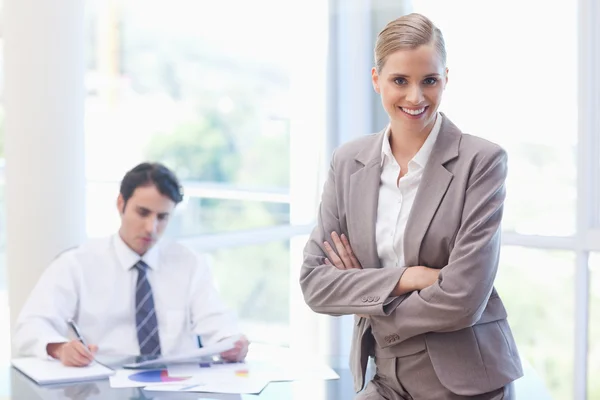 Lächelnde Geschäftsfrau posiert, während ihr Kollege arbeitet — Stockfoto
