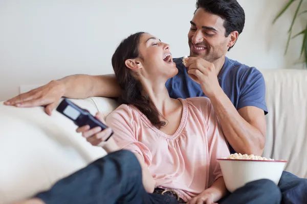Игривая пара смотрит телевизор, когда ест попкорн — стоковое фото