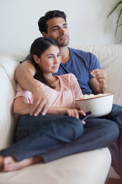 Портрет пары, смотрящей телевизор во время поедания попкорна — стоковое фото