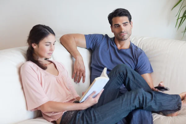 Женщина читает книгу, пока ее парень смотрит телевизор — стоковое фото
