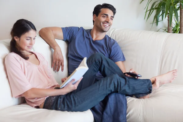 Woman reading a book while her husband is watching television — Stock Photo, Image