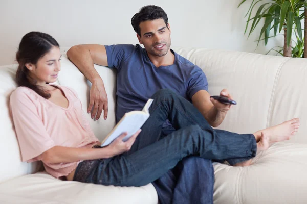 Woman reading a book while her fiance is watching television — Stock Photo, Image