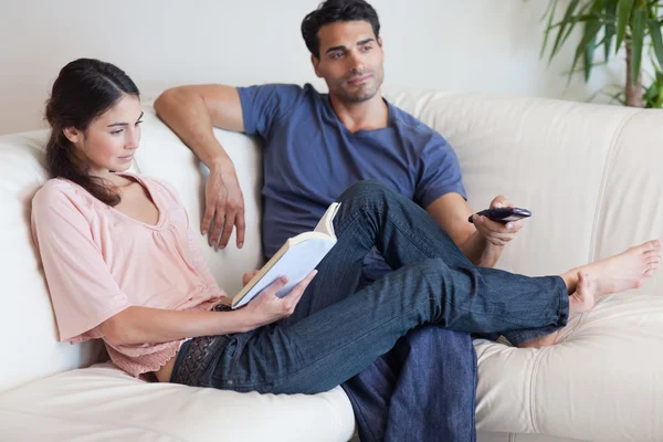 Woman reading a book while her fiance is watching TV — Stock Photo, Image