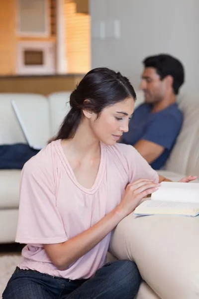 Portrait of a woman reading a book while her husband is using a — Stock Photo, Image