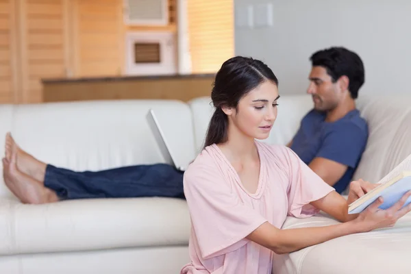 Woman reading a book while her fiance is using a laptop — Stock Photo, Image