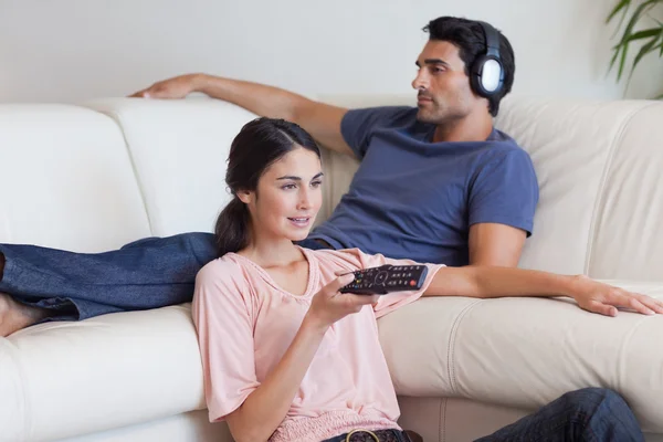 Женщина смотрит телевизор, пока ее жених слушает музыку — стоковое фото