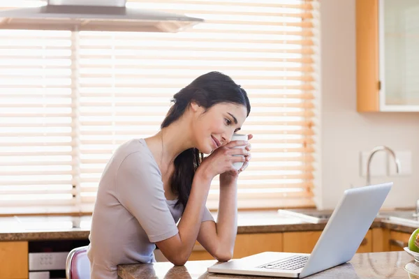 Güzel kadın bir çay yudumlarken bir dizüstü bilgisayar kullanarak — Stok fotoğraf