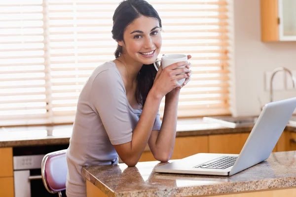Γοητευτική γυναίκα χρησιμοποιώντας ένα φορητό υπολογιστή, πίνοντας ένα φλιτζάνι του καφέ — Φωτογραφία Αρχείου