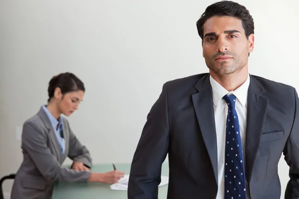 Schöner Geschäftsmann posiert, während sein Kollege arbeitet — Stockfoto