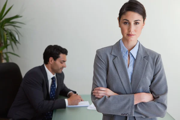 Professionelle Geschäftsfrau posiert, während ihr Kollege arbeitet — Stockfoto
