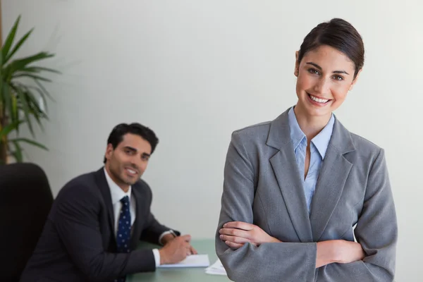 Glückliche Geschäftsfrau posiert, während ihr Kollege arbeitet — Stockfoto
