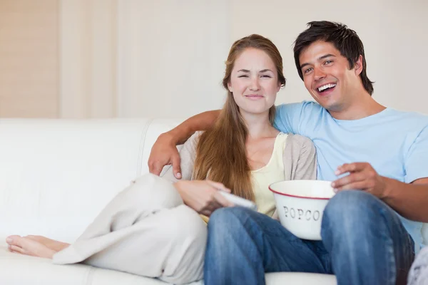 Улыбающаяся пара смотрит телевизор, когда ест попкорн — стоковое фото