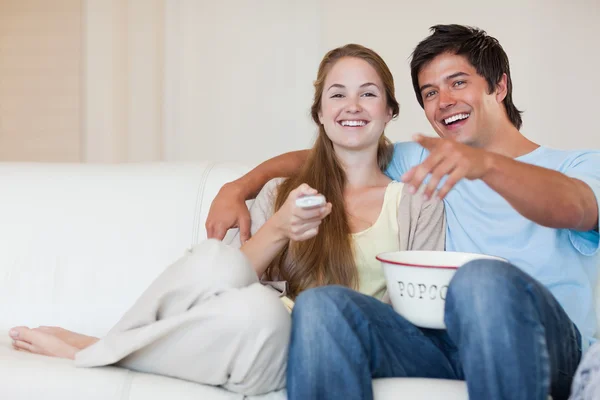 Casal rindo assistindo televisão enquanto come pipocas — Fotografia de Stock