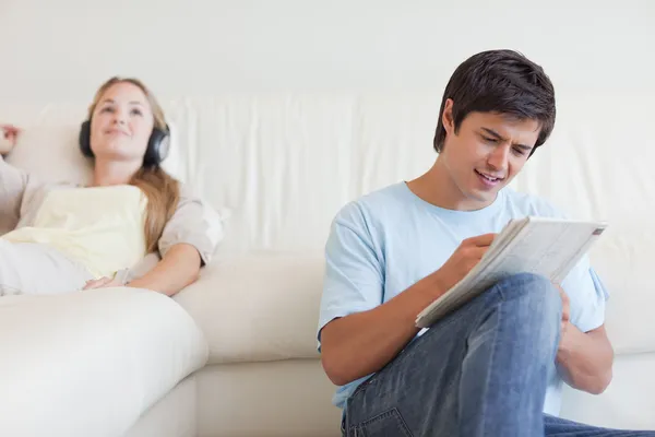 Man doing crosswords while his wife is listening to music — Stock Photo, Image