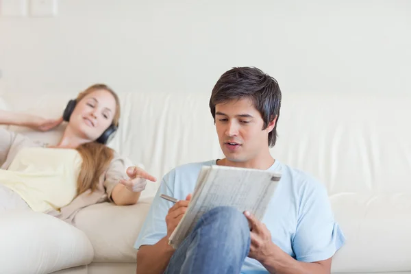 Woman helping her fiance to do crosswords while listening to mus — Stock Photo, Image