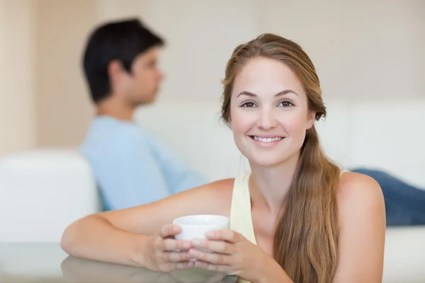 Žena pije čaj, zatímco její snoubenec sedí na gauči — Stock fotografie