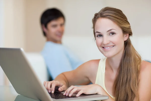 Woman using a laptop while her husband is sitting on a couch — Stock Photo, Image