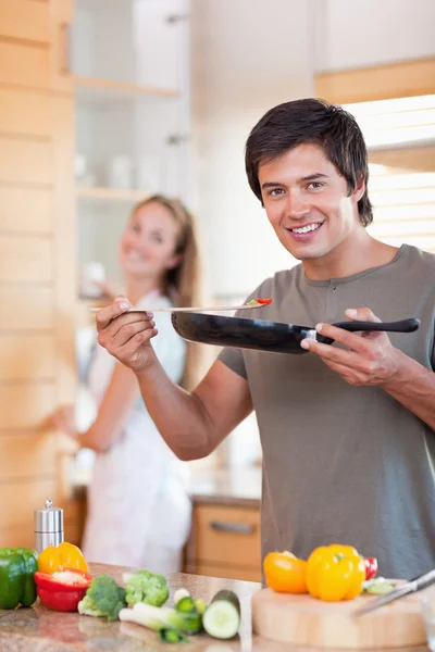 Retrato de um jovem cozinhando enquanto sua esposa está lavando o di — Fotografia de Stock