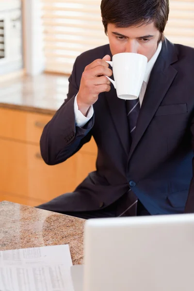 Portrait of a businessman drinking coffee while using a laptop — Stock Photo, Image