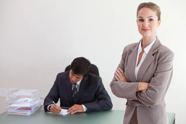 Junge Geschäftsfrau posiert, während ihr Kollege arbeitet — Stockfoto