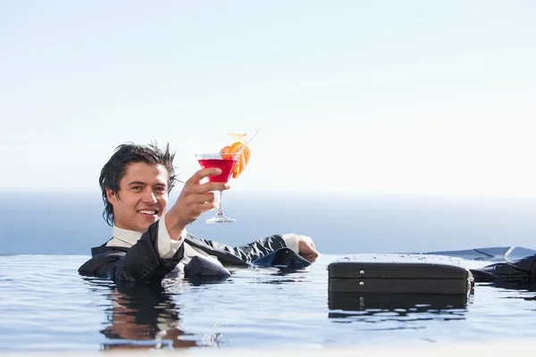 Cheerful businessman relaxing in a swimming pool with a cocktail — Stock Photo, Image