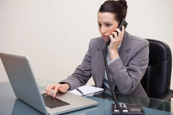 Empresária digitando em seu laptop enquanto no telefone — Fotografia de Stock
