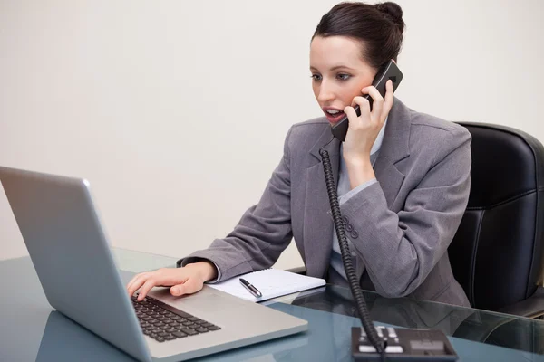 Empresária digitando no laptop enquanto fala no telefone — Fotografia de Stock